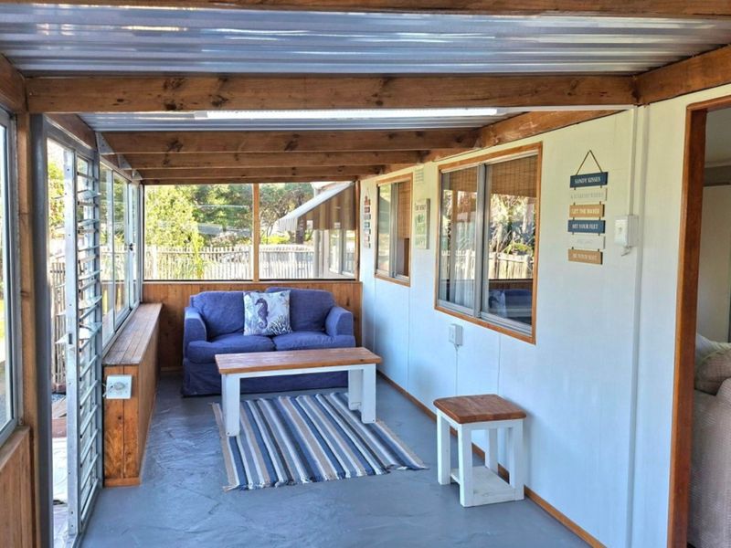 A covered patio area featuring exposed timber beams, a corrugated metal roof, and large louvre windows overlooking the garden.