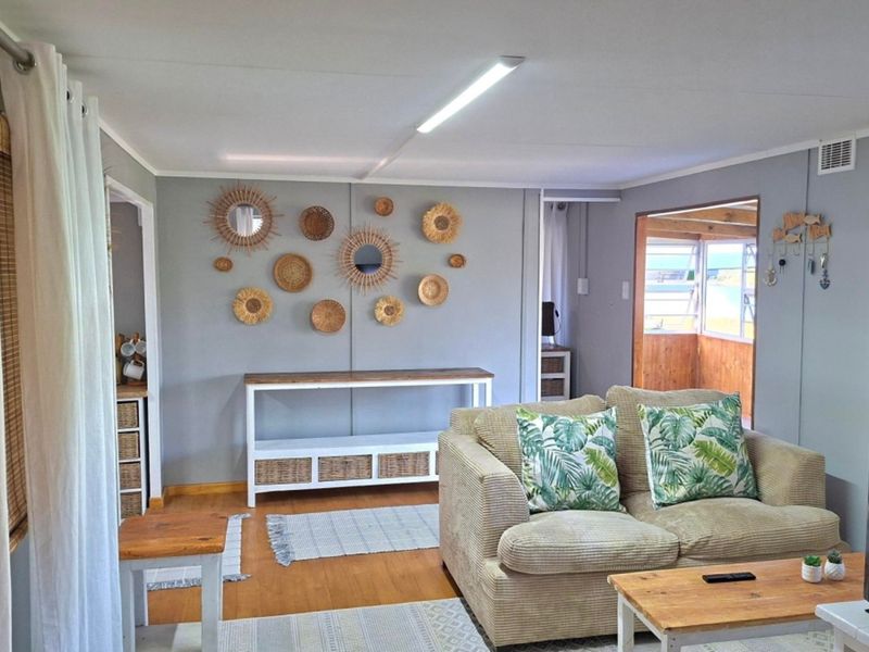 A comfortable living room featuring laminate flooring and neutral wall tones, with an open flow leading into an adjacent sunroom area.