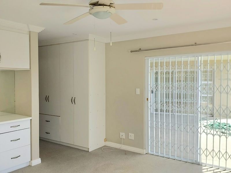 Spacious bedroom featuring built-in cupboards, a vanity unit, ceiling fan, and a sliding door with a security gate leading to the patio.