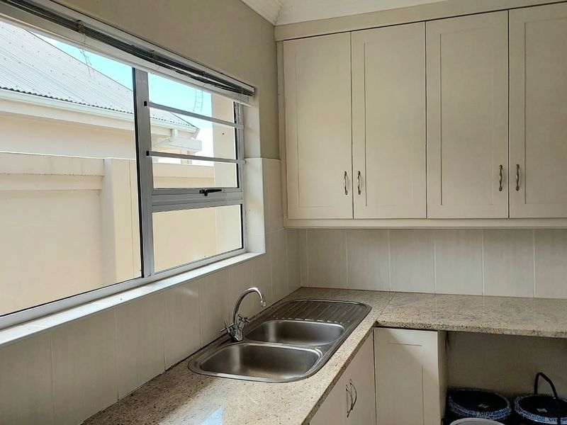 A functional scullery area featuring granite countertops, a double bowl stainless steel sink, and ample built-in cabinetry for storage.