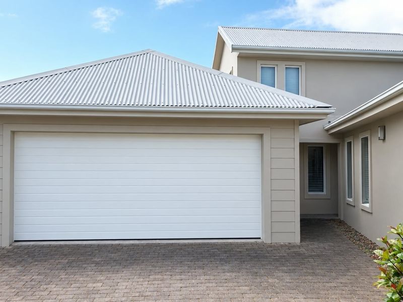 Front elevation of a townhouse featuring a clean sectional garage door, corrugated metal roofing, and a paved driveway area.