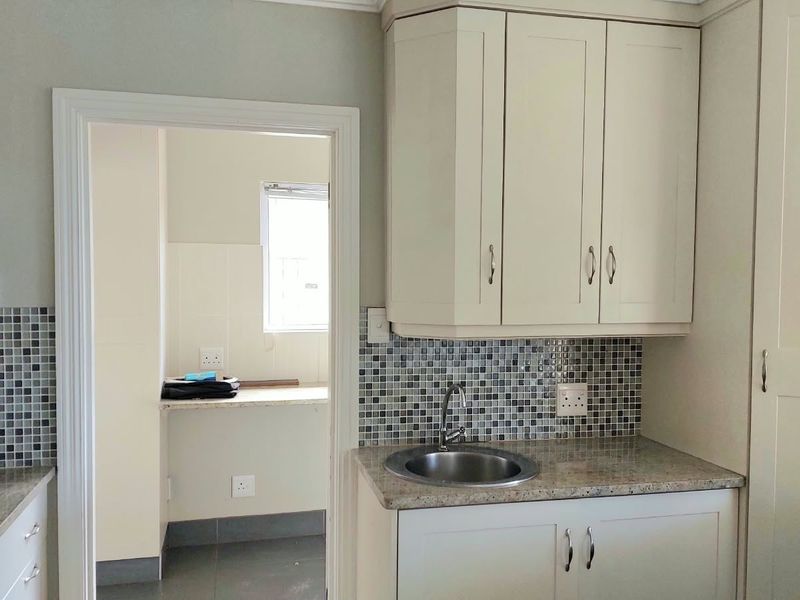 A functional scullery area featuring built-in cabinetry, granite countertops, a stainless steel sink, and a decorative mosaic tile backsplash.