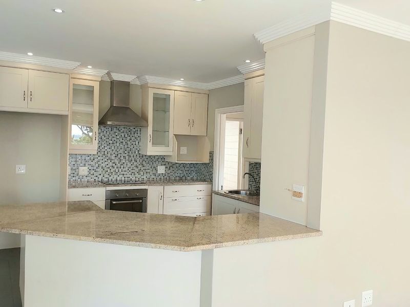A clean, functional kitchen featuring granite countertops, a mosaic tile backsplash, built-in oven, extractor fan, and ample cabinetry with crown molding details.