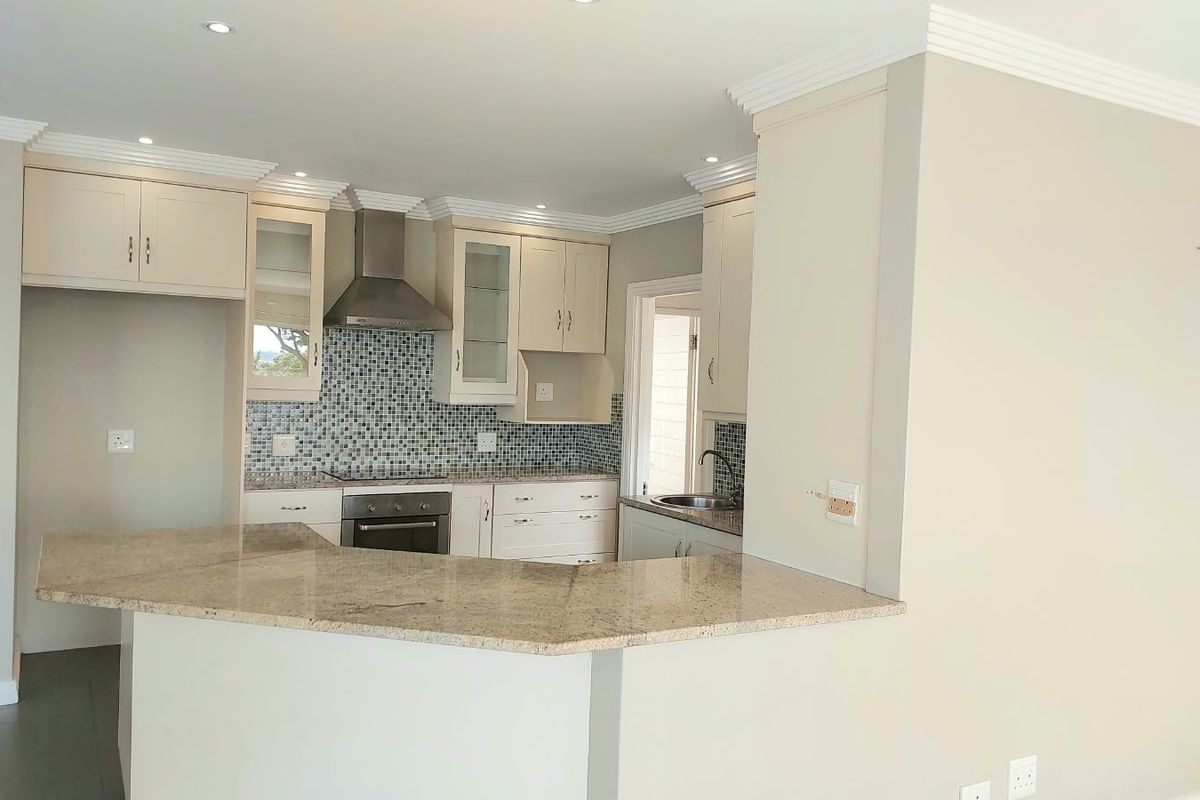 A clean, functional kitchen featuring granite countertops, a mosaic tile backsplash, built-in oven, extractor fan, and ample cabinetry with crown molding details.