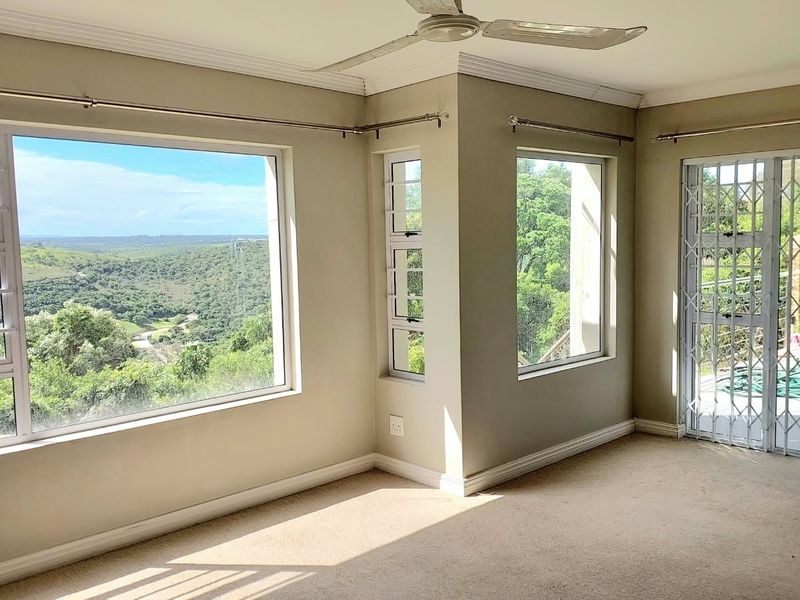 Bright and spacious living area featuring large windows with scenic views, neutral carpeting, and a ceiling fan, offering a blank canvas for interior design.