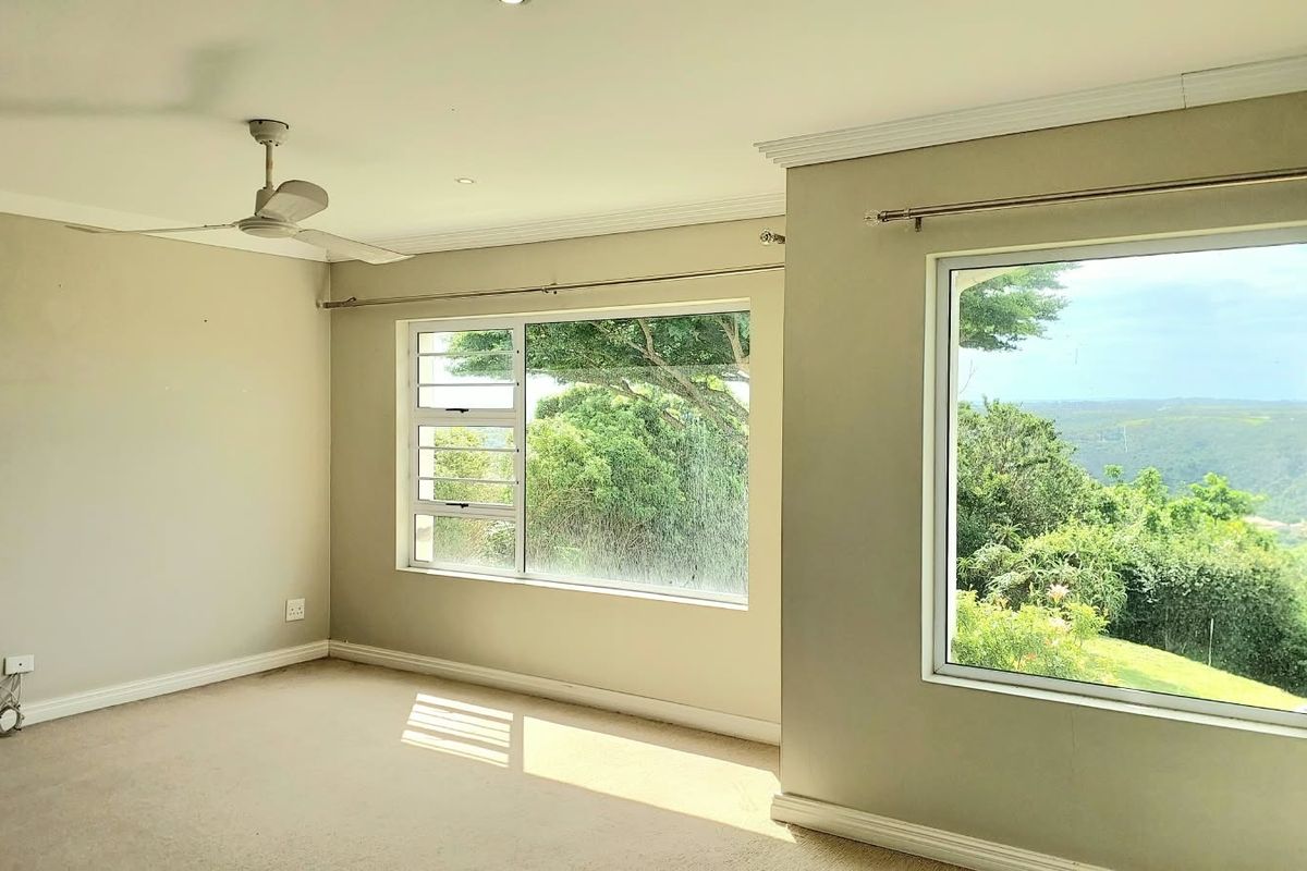 A bright, empty bedroom featuring neutral walls, carpeted flooring, recessed lighting, a ceiling fan, and large windows offering scenic views.