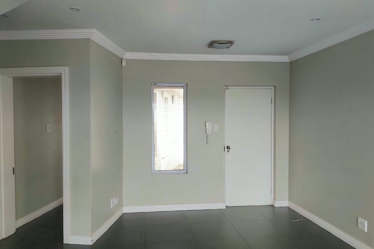 An empty living area featuring neutral wall tones, tiled flooring, crown molding, and recessed lighting, providing a clean and versatile space.