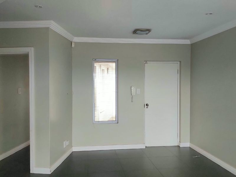 An empty living area featuring neutral wall tones, tiled flooring, crown molding, and recessed lighting, providing a clean and versatile space.