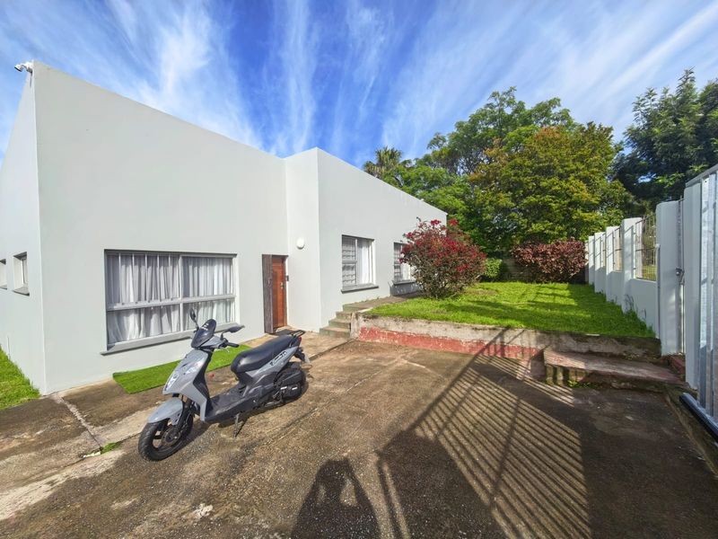 Rear exterior view of the property featuring a concrete driveway, a small lawn area, and a retaining wall.