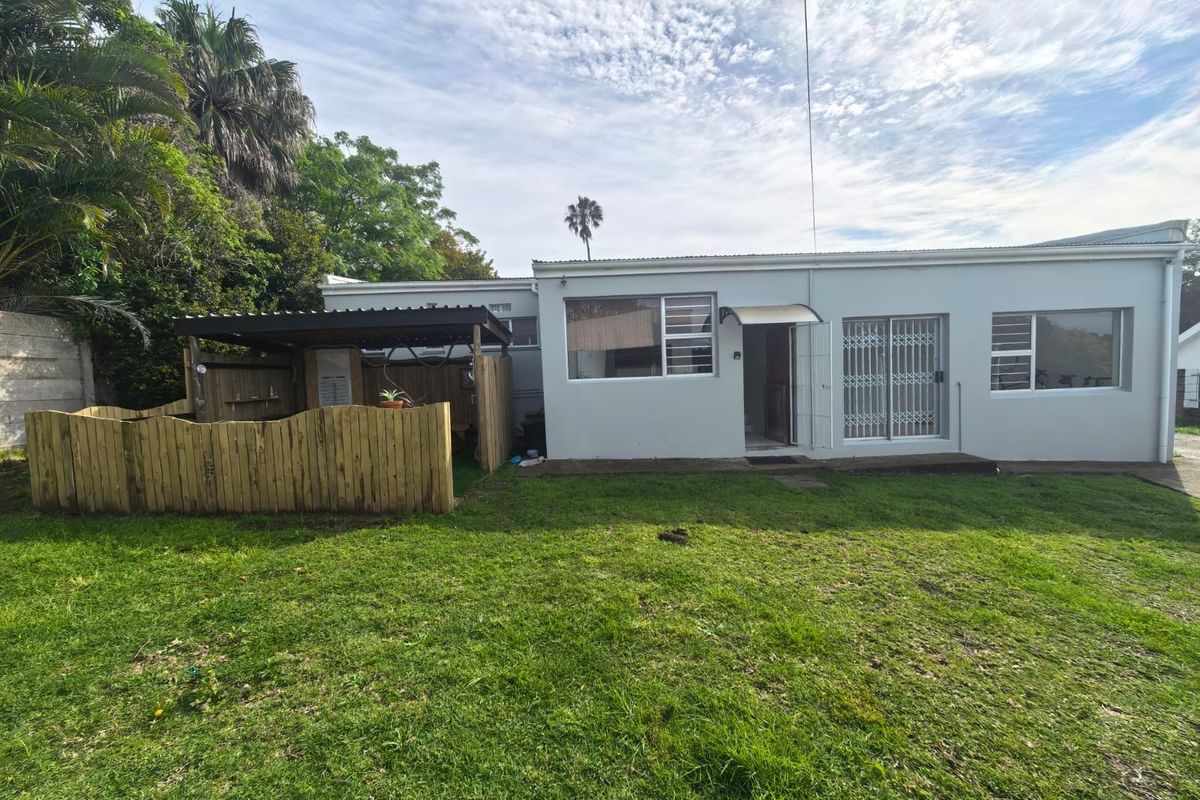 Rear view of the property featuring a lawn, a timber fenced area, and a covered patio space with sliding glass doors.