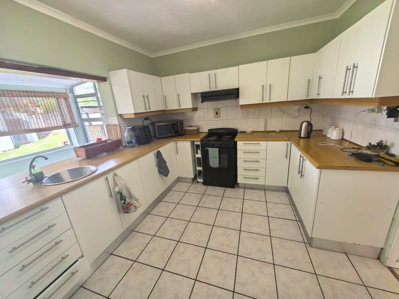 A functional kitchen featuring white cabinetry, wooden countertops, tiled flooring, and a built-in extractor fan, offering a practical layout for daily meal preparation.