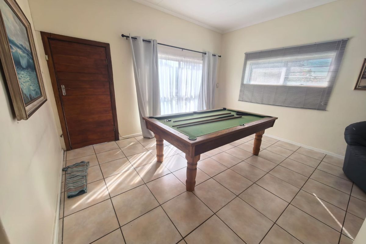 A versatile living area featuring neutral tiled flooring, a solid timber door, and natural light through window blinds and curtains.