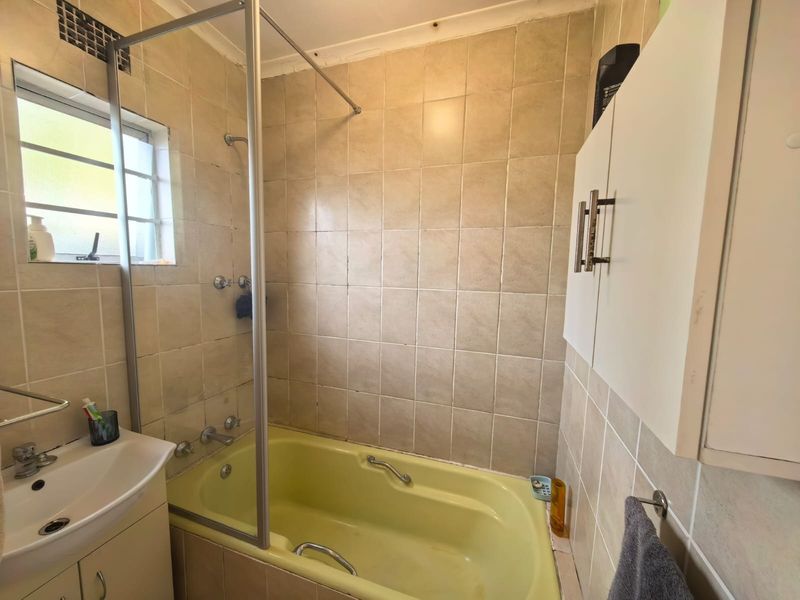 A compact bathroom featuring a yellow bathtub, tiled walls, a built-in vanity, and a wall-mounted storage cabinet.