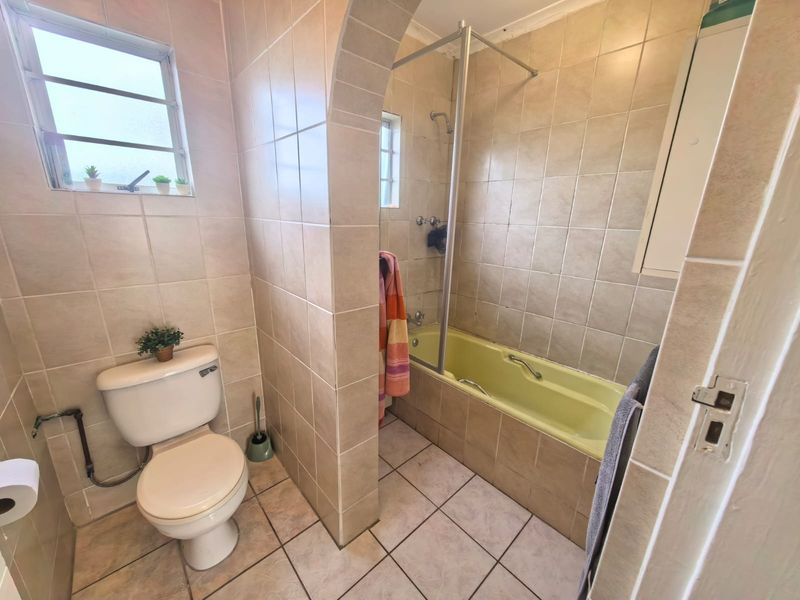A functional bathroom featuring tiled walls and flooring, a built-in bathtub with a shower screen, and a separate toilet area.