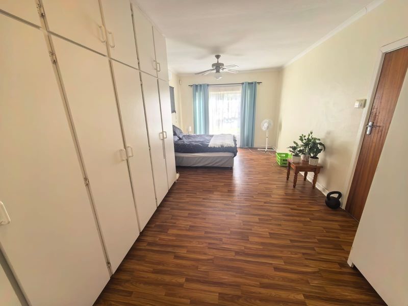 Spacious bedroom featuring extensive built-in cupboards, laminate flooring, and a ceiling fan, with direct access to the outdoors via a sliding door.