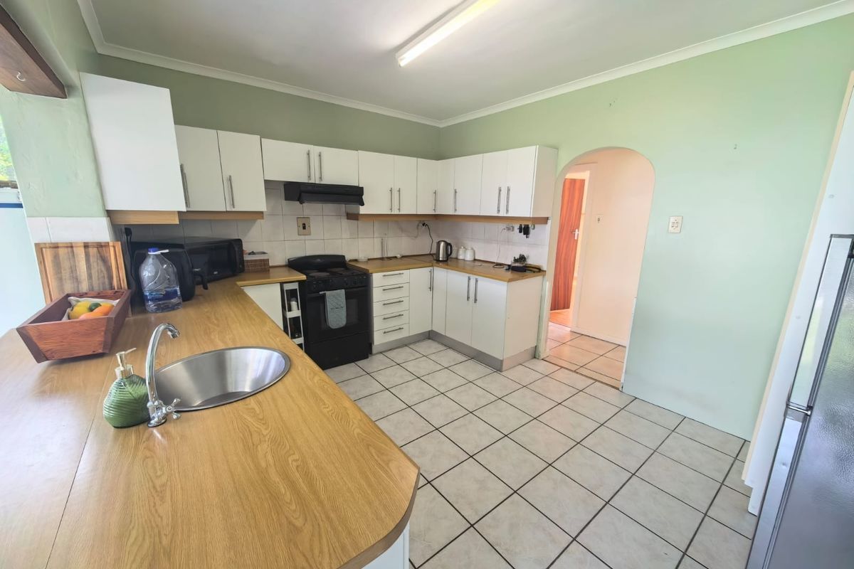 Functional kitchen featuring white cabinetry, laminate countertops, stainless steel sink, and tiled flooring, with an arched doorway leading to adjacent living spaces.