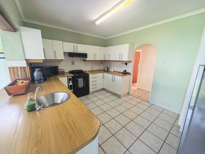 Functional kitchen featuring white cabinetry, laminate countertops, stainless steel sink, and tiled flooring, with an arched doorway leading to adjacent living spaces.