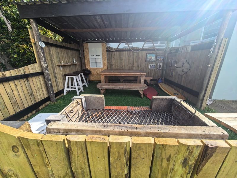 Covered outdoor entertainment area featuring a built-in braai, timber pergola structure, and fenced perimeter, ideal for casual alfresco dining and social gatherings.