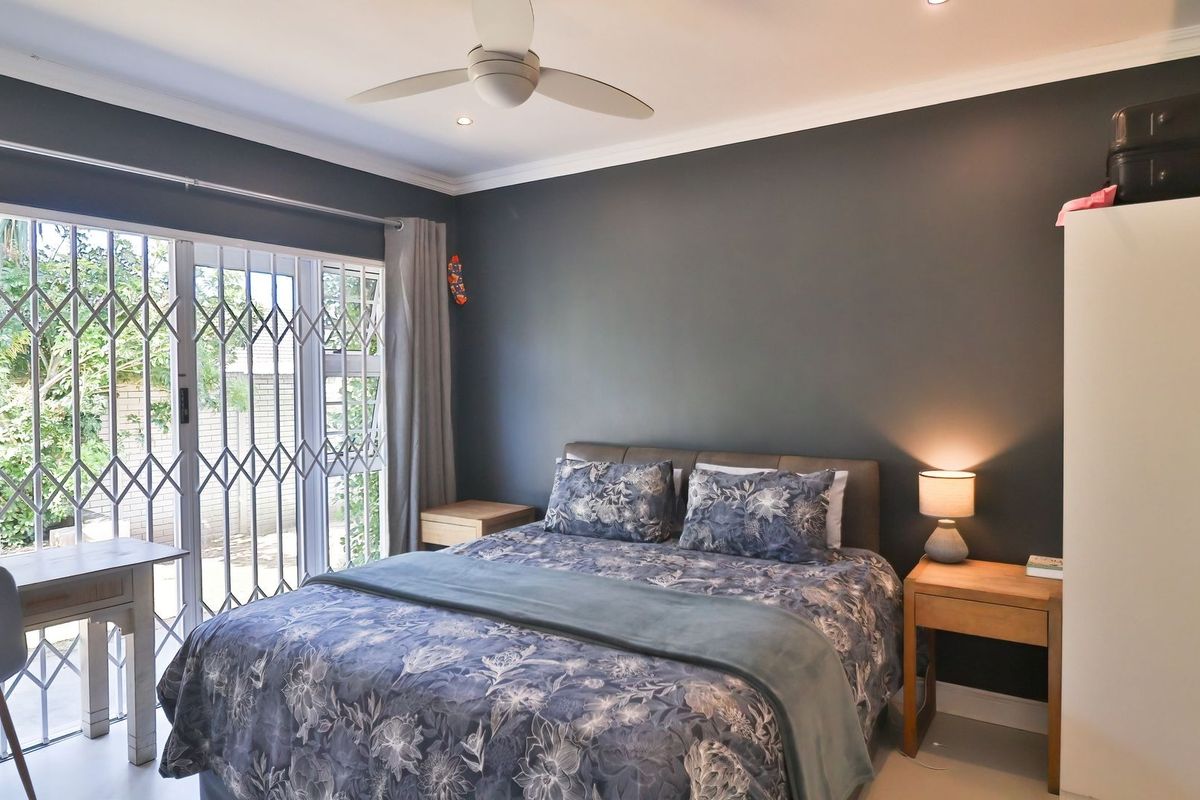 A well-maintained bedroom featuring dark accent walls, a ceiling fan, and sliding glass doors with security gates leading to the exterior.
