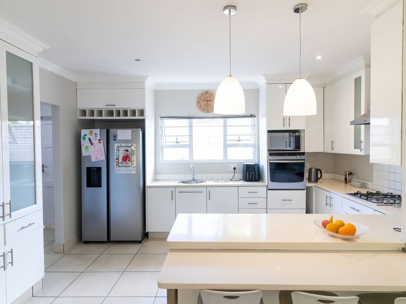 A bright, modern kitchen featuring white cabinetry, stone countertops, integrated appliances, and a functional breakfast bar with pendant lighting.