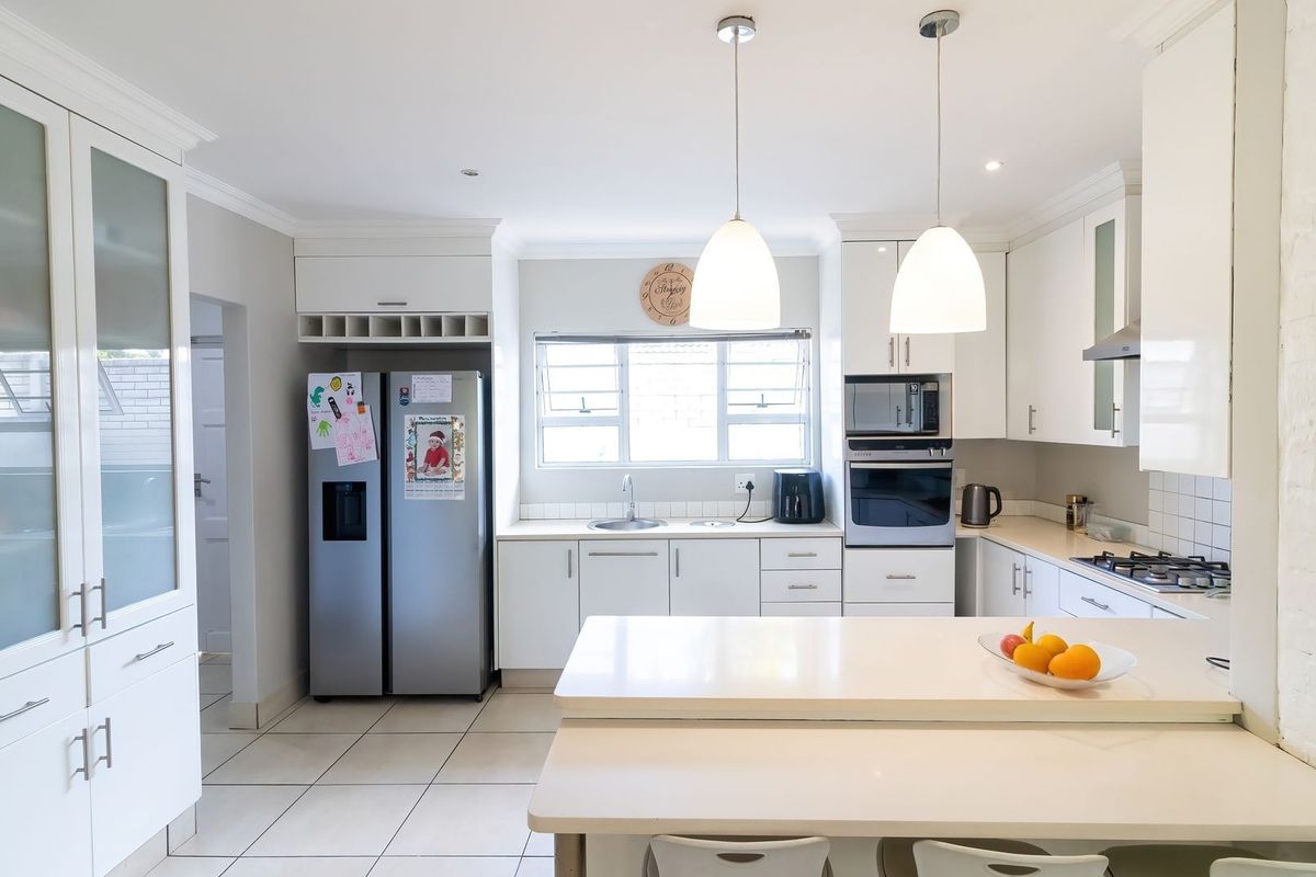 A bright, modern kitchen featuring white cabinetry, stone countertops, integrated appliances, and a functional breakfast bar with pendant lighting.