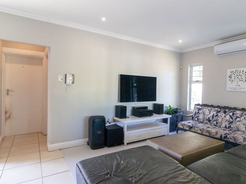 A well-maintained living room featuring neutral walls, tiled flooring, coving, and a wall-mounted air conditioning unit.