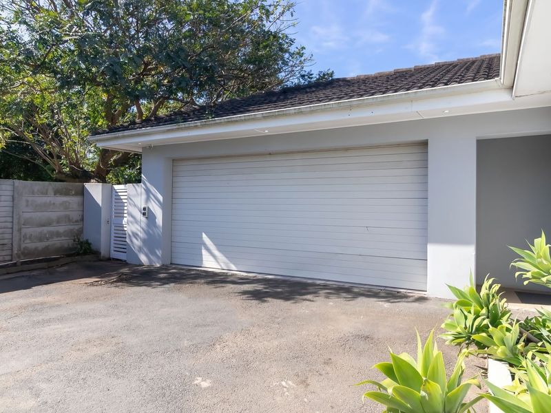 Exterior view of a double garage featuring a white automated door, paved driveway, and surrounding boundary walling.