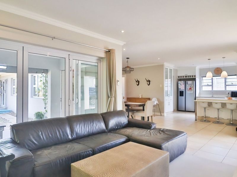 Spacious open-plan living area featuring tiled floors, recessed lighting, and a modern kitchen with a central island, seamlessly connecting to an outdoor patio.