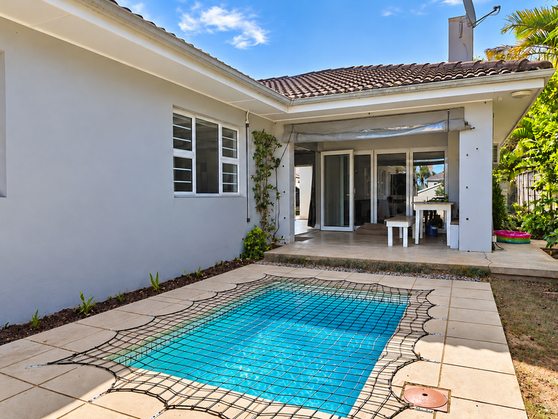Rear exterior view featuring a swimming pool with safety net, tiled pool deck, and a covered patio area with sliding glass door access.
