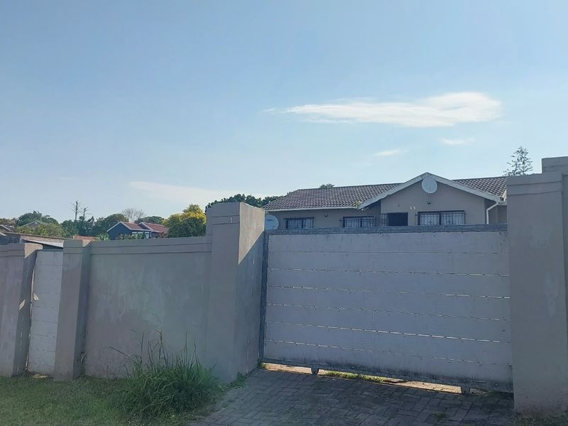 Front view of the property featuring a secure perimeter wall, sliding gate, and a tiled roof house with security bars on windows.