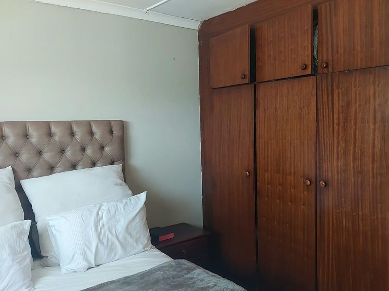 A bedroom featuring a large built-in wooden wardrobe with overhead storage compartments and neutral wall finishes.