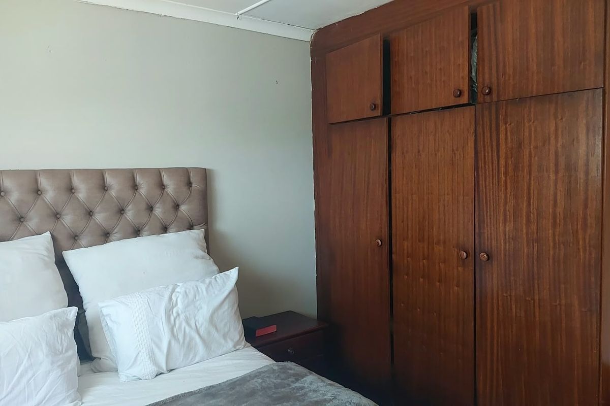 A bedroom featuring a large built-in wooden wardrobe with overhead storage compartments and neutral wall finishes.