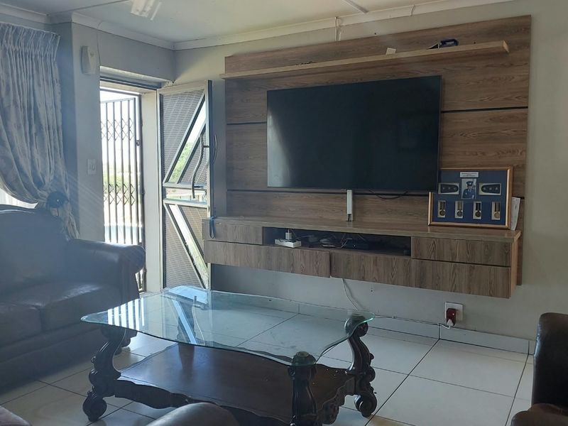 A living room featuring tiled flooring and a built-in wooden media unit with direct access to an exterior security gate.
