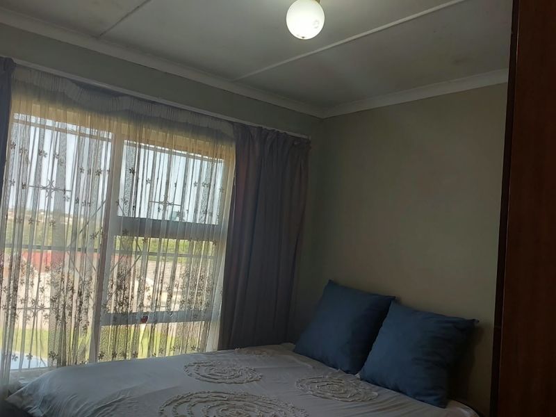 A functional bedroom featuring a large window with security bars and a built-in cupboard, offering a simple and practical living space.