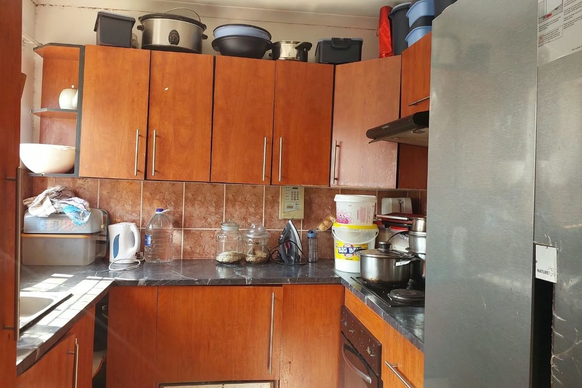 A functional kitchen featuring wood-look laminate cabinetry, dark countertops, and a tiled backsplash, equipped with a built-in oven, hob, and extractor fan.