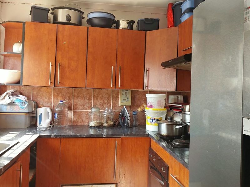 A functional kitchen featuring wood-look laminate cabinetry, dark countertops, and a tiled backsplash, equipped with a built-in oven, hob, and extractor fan.