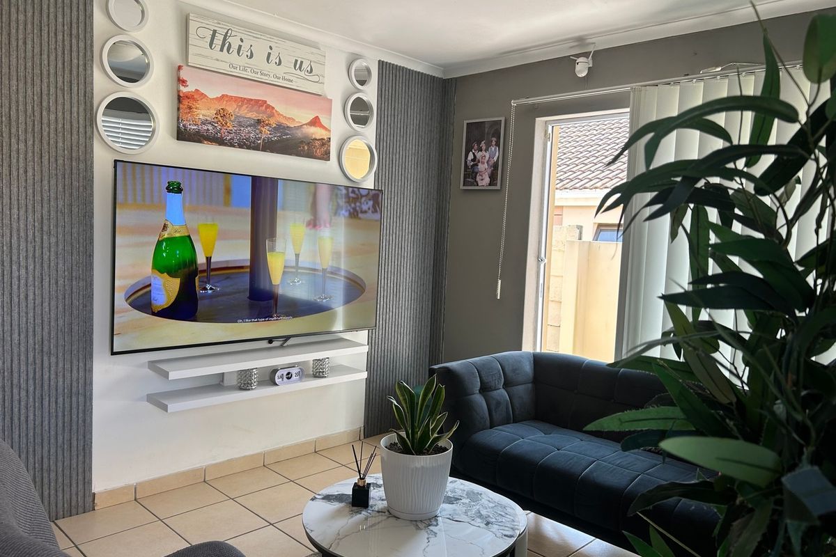 A cozy living room featuring decorative vertical wall paneling, floating shelves, and tiled flooring with natural light entering through a side window.