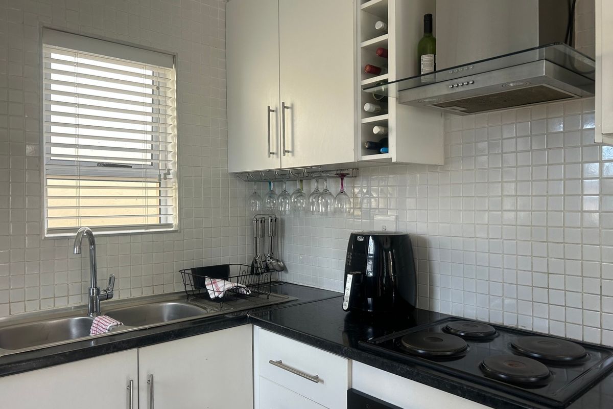 A functional kitchen featuring white cabinetry, black countertops, a double basin sink, and a built-in electric hob with an overhead extractor fan.