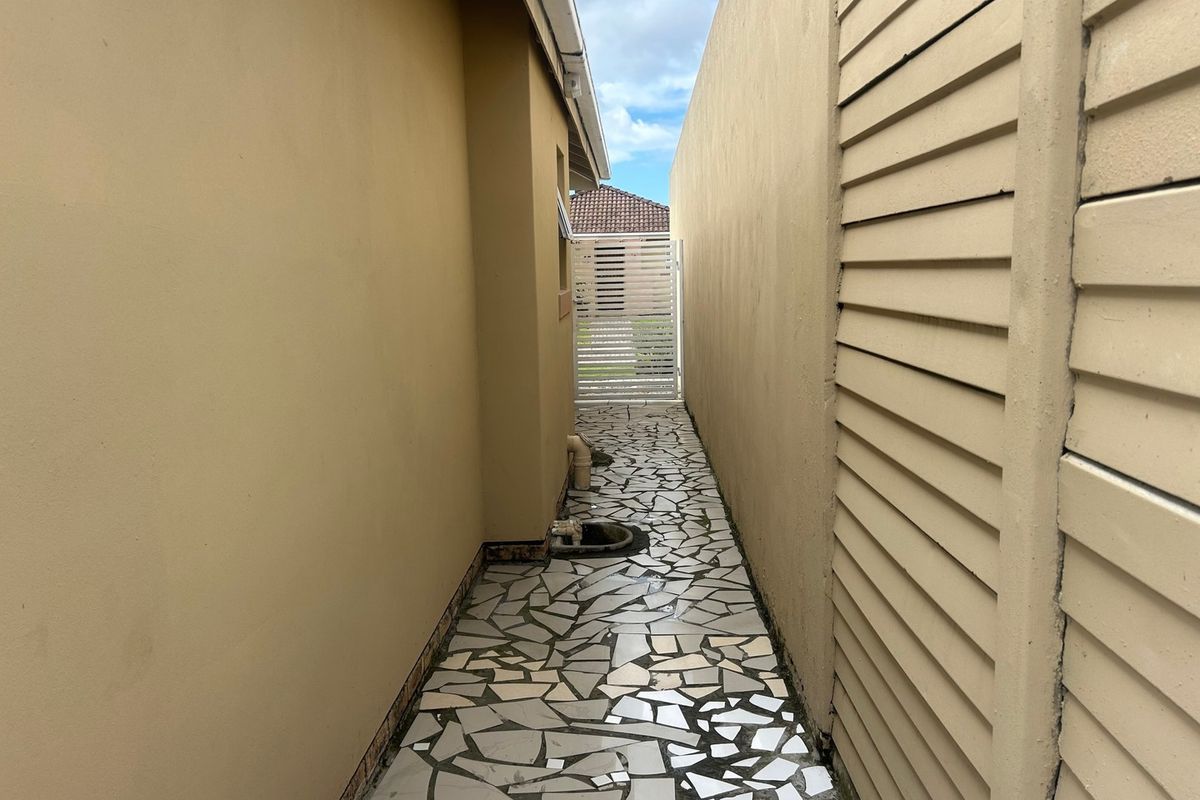 A narrow side passage or rear walkway featuring crazy paving, boundary walls, and a security gate.