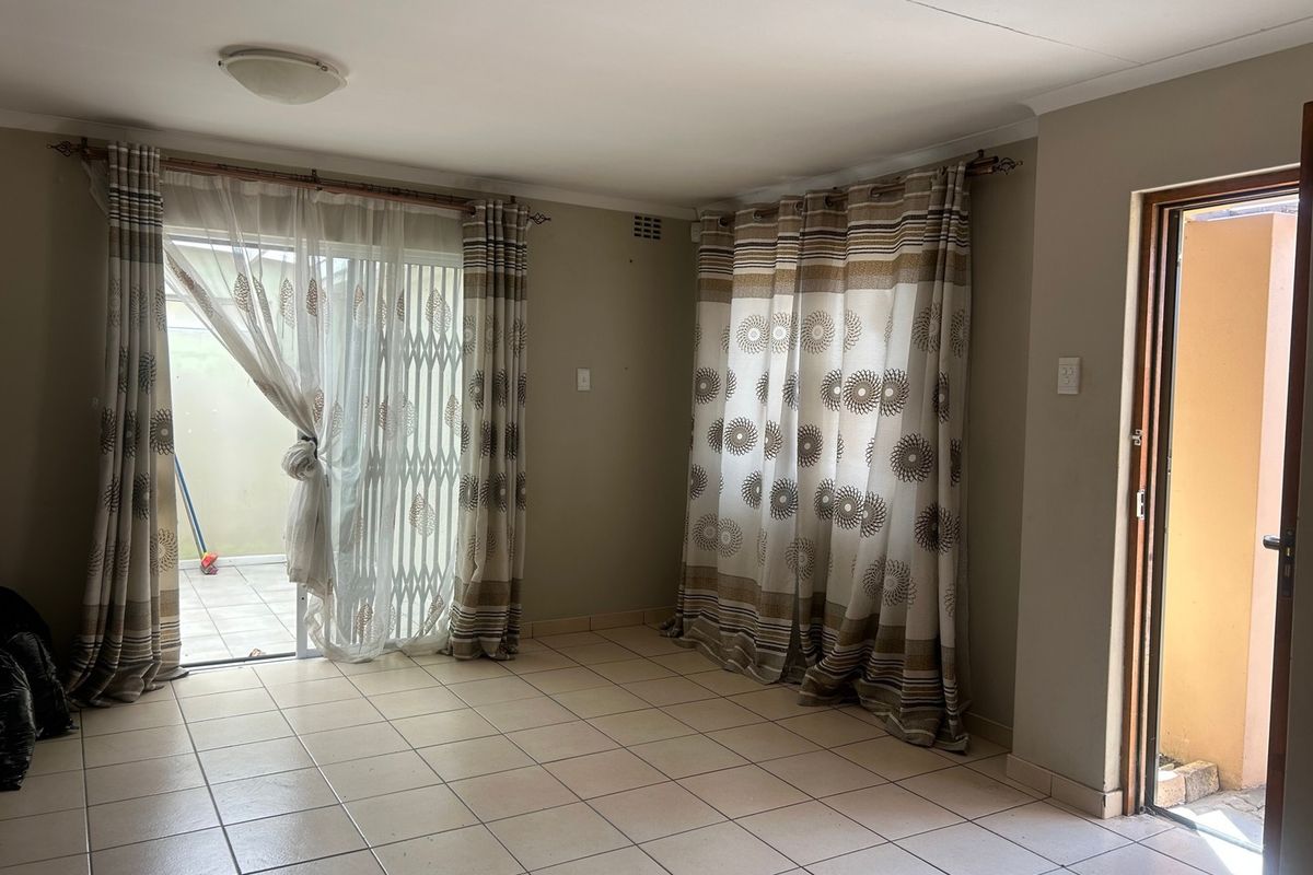 A bright, open-plan living area featuring neutral ceramic floor tiles, coving, and direct access to an outdoor patio through a sliding glass door.