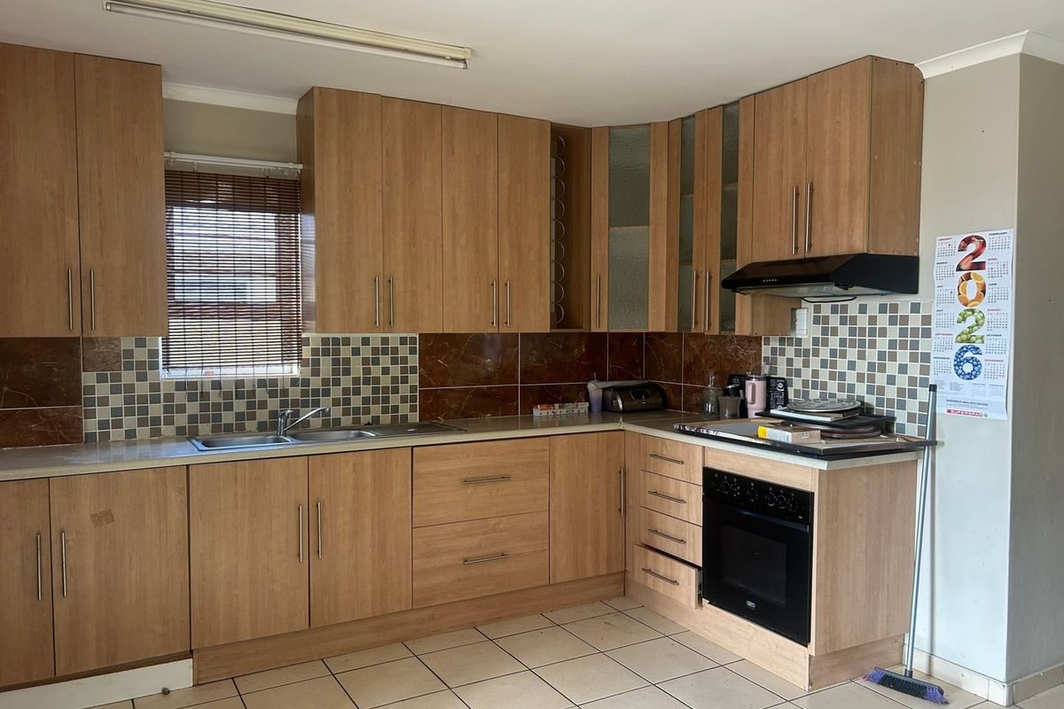 A functional kitchen featuring wood-look laminate cabinetry, built-in oven, extractor fan, double sink, and tiled splashback with neutral floor tiles.