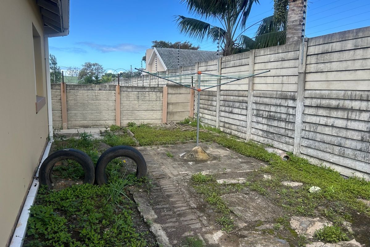 A rear courtyard area featuring a precast concrete boundary wall, paved sections, and a rotary clothesline, currently requiring landscaping and maintenance.