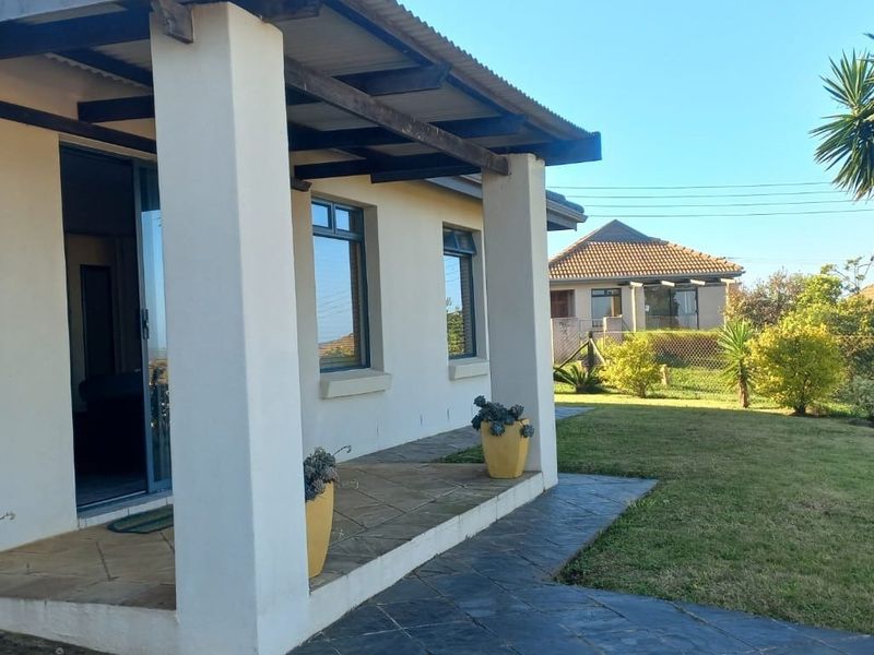A covered patio area featuring tiled flooring, concrete pillars, and exposed timber rafters, providing direct access to the garden through a sliding glass door.