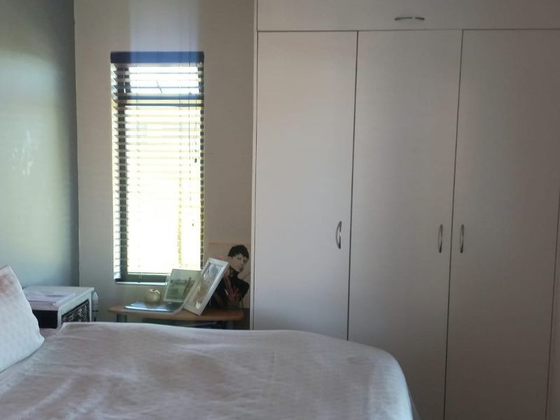 A bedroom featuring a built-in wardrobe with white doors and a window fitted with venetian blinds.