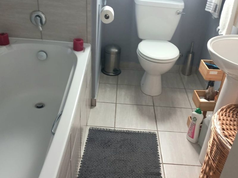A functional bathroom featuring a built-in bathtub, pedestal basin, and toilet with neutral tiled finishes throughout.