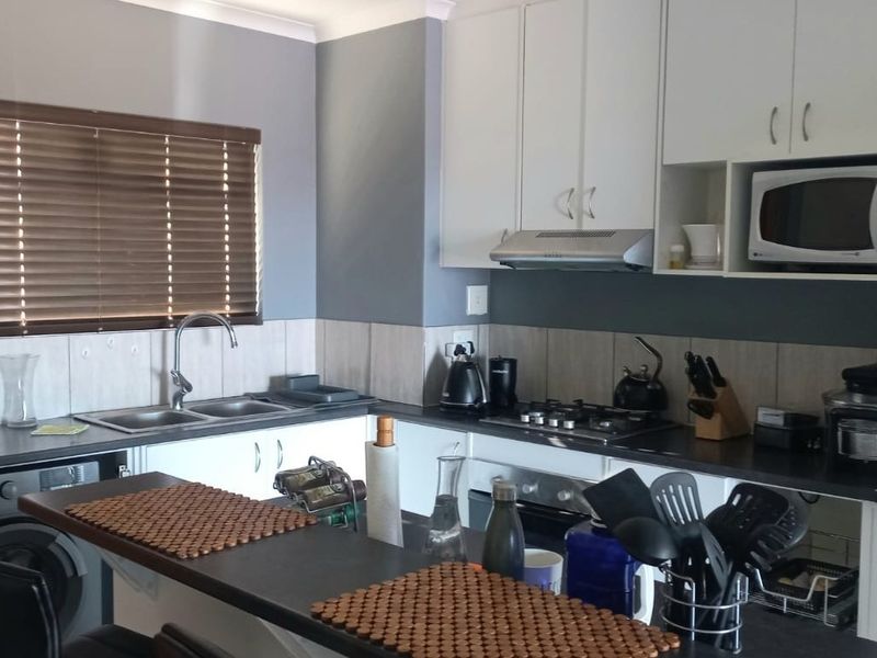 A functional kitchen featuring white cabinetry, dark countertops, a gas hob with extractor, and a double sink with a tiled backsplash.