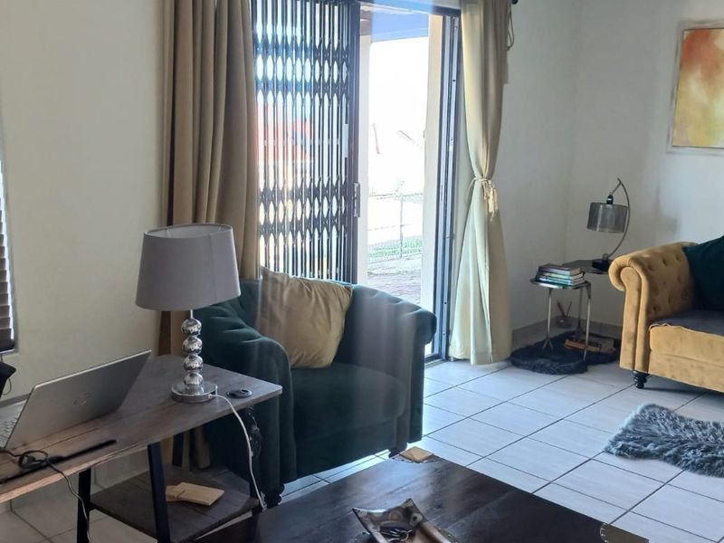 A living room featuring tiled flooring, venetian blinds, and a sliding glass door with a security gate leading to the exterior.