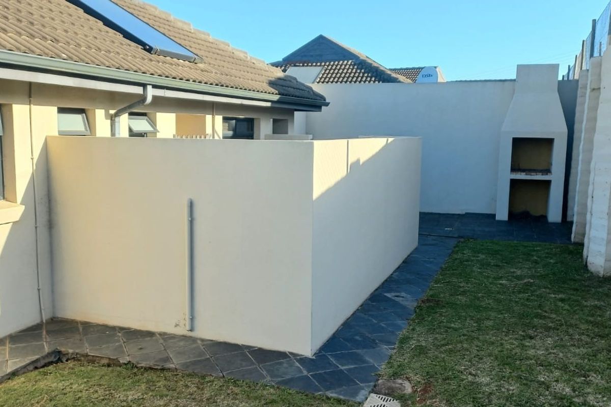 Rear exterior view featuring a paved patio area, a built-in braai, and a small garden space with boundary walling.