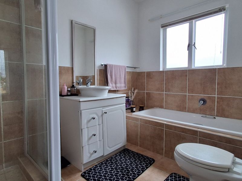 A functional bathroom featuring a shower enclosure, built-in bathtub, vanity with vessel sink, and neutral wall tiling.