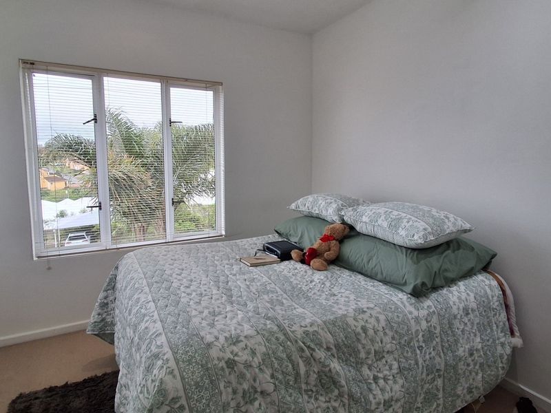 A simple bedroom featuring a large window with venetian blinds, providing natural light and an exterior view.